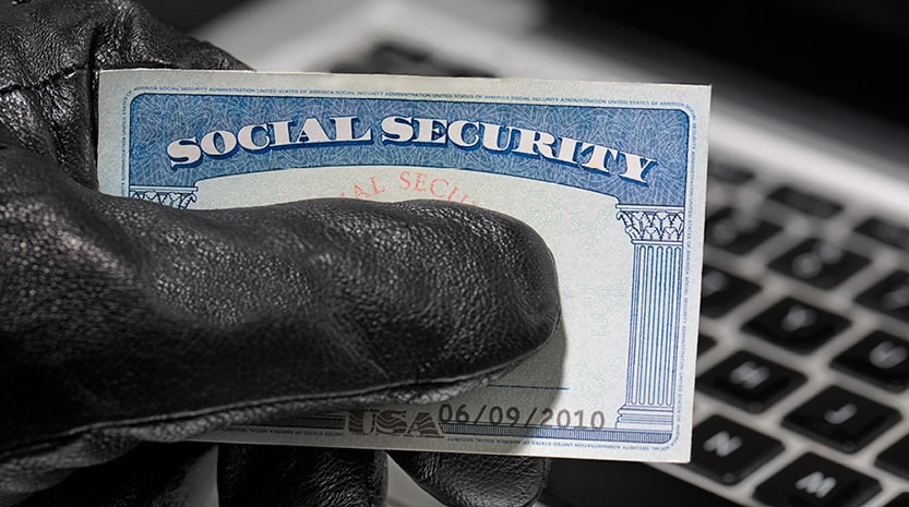 A hand wearing a black leather glove holds a social security card over a laptop keyboard.