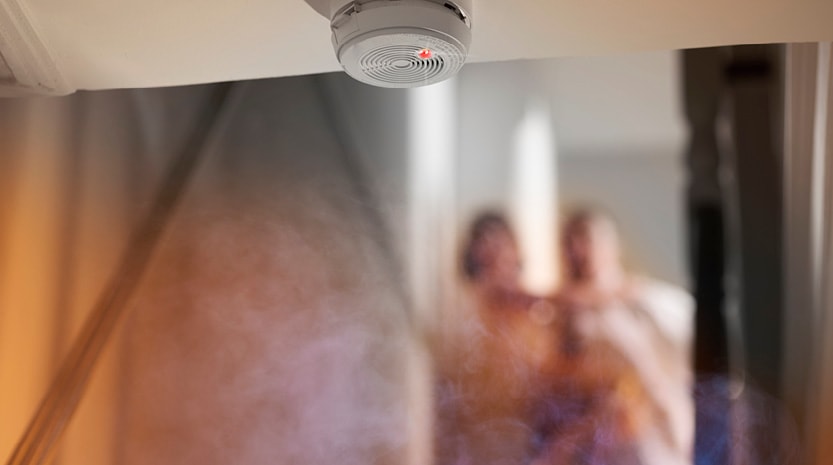 Two people looking at a smoke detector on the ceiling.