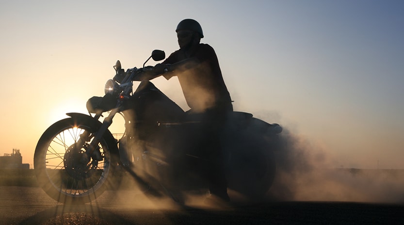 A silhouette of a man on a motorcycle at sunset.